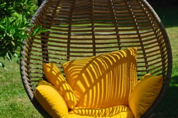 One of the outdoor swing ideas is a wicker egg chair, like this one, which has a yellow cushion